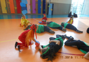 Grupa dzieci w kolorowych strojach wykonuje taniec w pozycji kucznej.